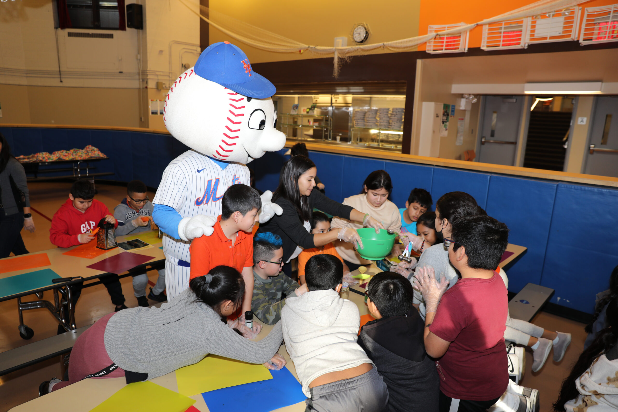 kids sitting at a table talking to a man with a baseball costume on